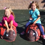 Little girls sit on custom ladybug seats in inclusive playground