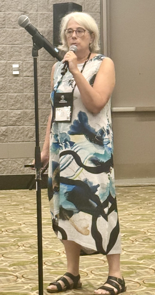 Mara standing at a microphone in a conference room.